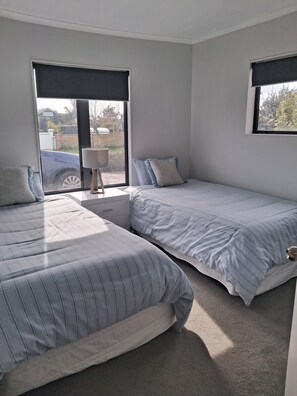 A bedroom with two beds, a bedside table, a lamp, and a window with a view of the outside. - 2-minutes walk to the beach, Spacious Home and great outdoor living. (Tauranga)