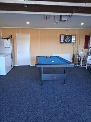 A pool table with balls, a refrigerator, a door, and dartboards on the wall. - 2-minutes walk to the beach, Spacious Home and great outdoor living. (Tauranga)
