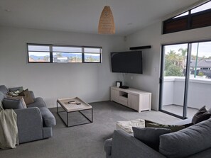 A modern living room with a grey sofa, a coffee table, and a TV on a white stand. - 2-minutes walk to the beach, Spacious Home and great outdoor living. (Tauranga)