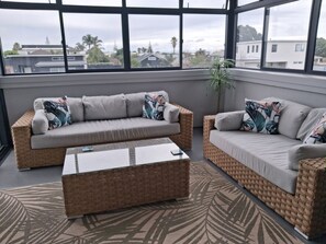 A modern living room with two sofas, a coffee table, and a large window offering a view of buildings and trees. - 2-minutes walk to the beach, Spacious Home and great outdoor living. (Tauranga)
