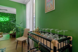A room with a green wall, a wooden chair, a glass table with wine glasses, and a neon sign. - 4 Min to Beach! 85°F Pool•Sauna•Golf•Pickleball (Seminole)