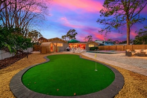 Ein Garten mit Putting Green, Pool und einer Terrasse mit Sitzgelegenheiten.