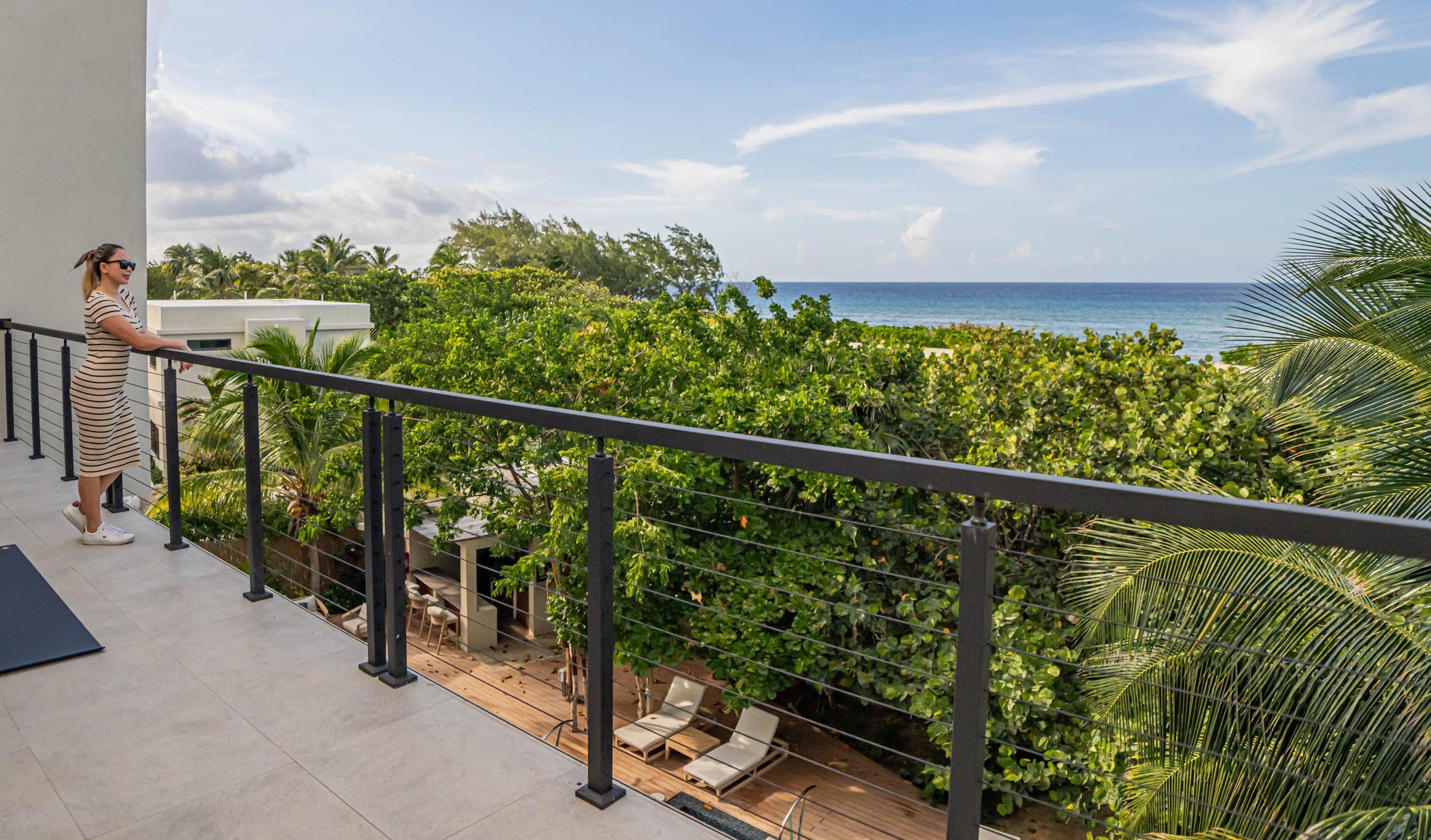 A balcony with a view of the ocean, surrounded by lush greenery.