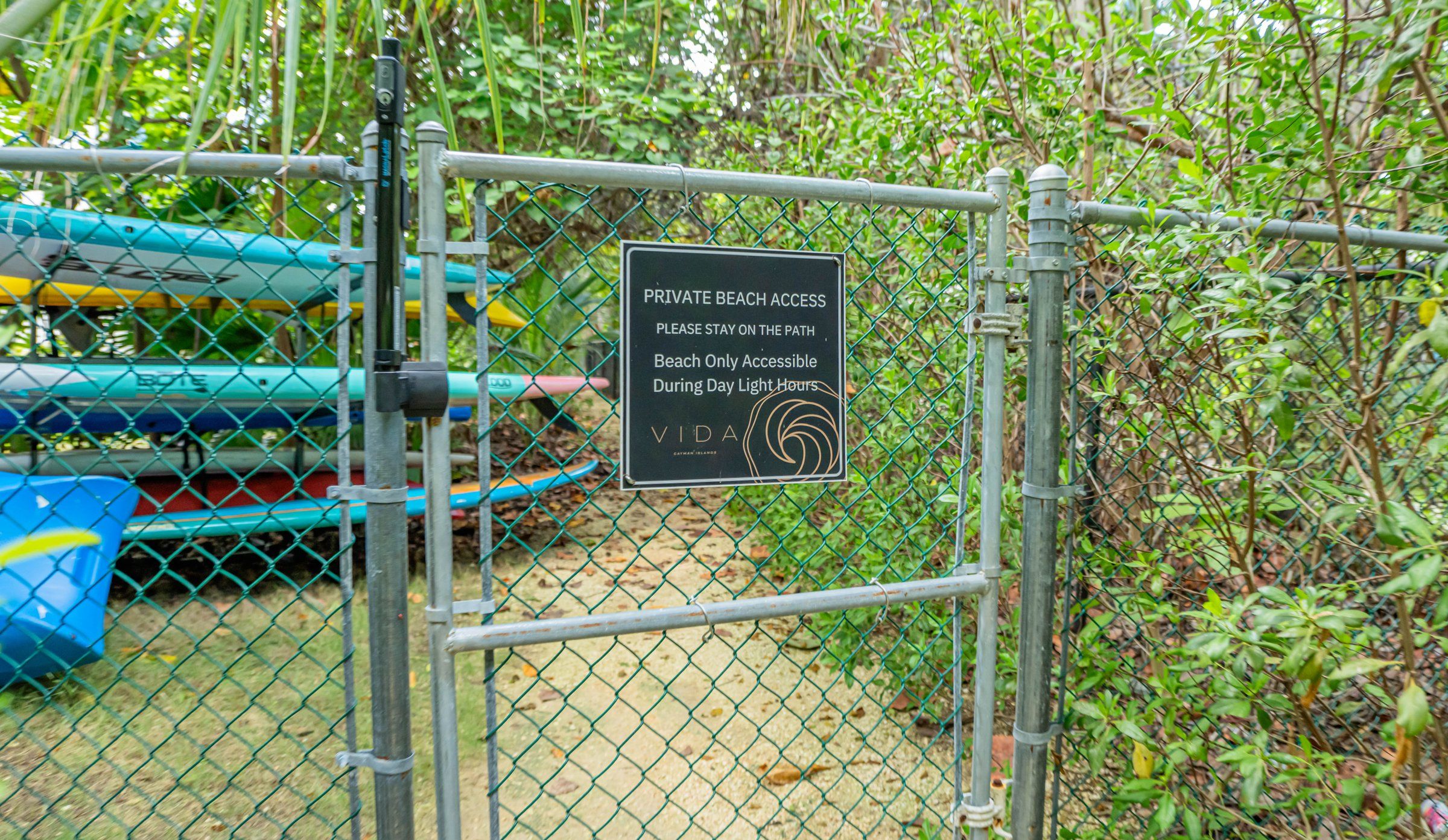 A chain-link fence with a sign indicating private beach access and a path to stay on.