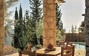 An outdoor dining area with stone pillars, wooden chairs, a table, and a lamp. - Cozy home in Lefkada with private swimming pool, can be inside or outside (Lefkada)