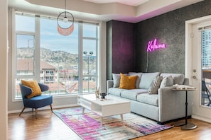 A modern living room with a large window, a sofa, a coffee table, and a neon sign. - Lakeside Escape - Year round pool and hot tub - seasonal tennis courts (Kelowna)