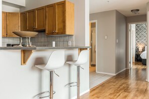 A kitchen with wooden cabinets, a countertop, and two white bar stools. - Lakeside Escape - Year round pool and hot tub - seasonal tennis courts (Kelowna)