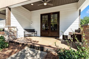 A covered porch with a wooden bench, a door, and outdoor furniture. - Southern Row | Two King Bedrooms | Walk to UA (Tuscaloosa)
