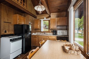 Een keuken met houten kastjes, een fornuis, een koelkast en een eettafel met stoelen.