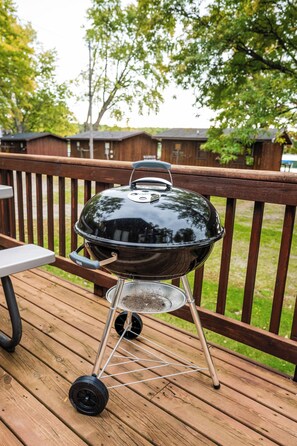 A portable barbecue grill on a wooden deck with a metal table and a metal chair nearby. - Seehaus at Sommer Dorf (West Branch)