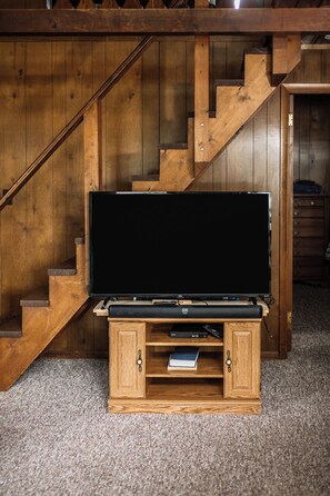 A wooden entertainment unit with a flat-screen TV, located in a room with wooden stairs. - Seehaus at Sommer Dorf (West Branch)
