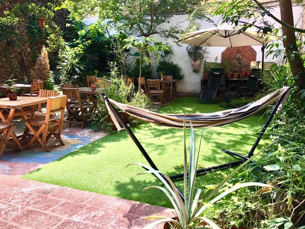 A garden patio with a hammock, wooden tables, and chairs.