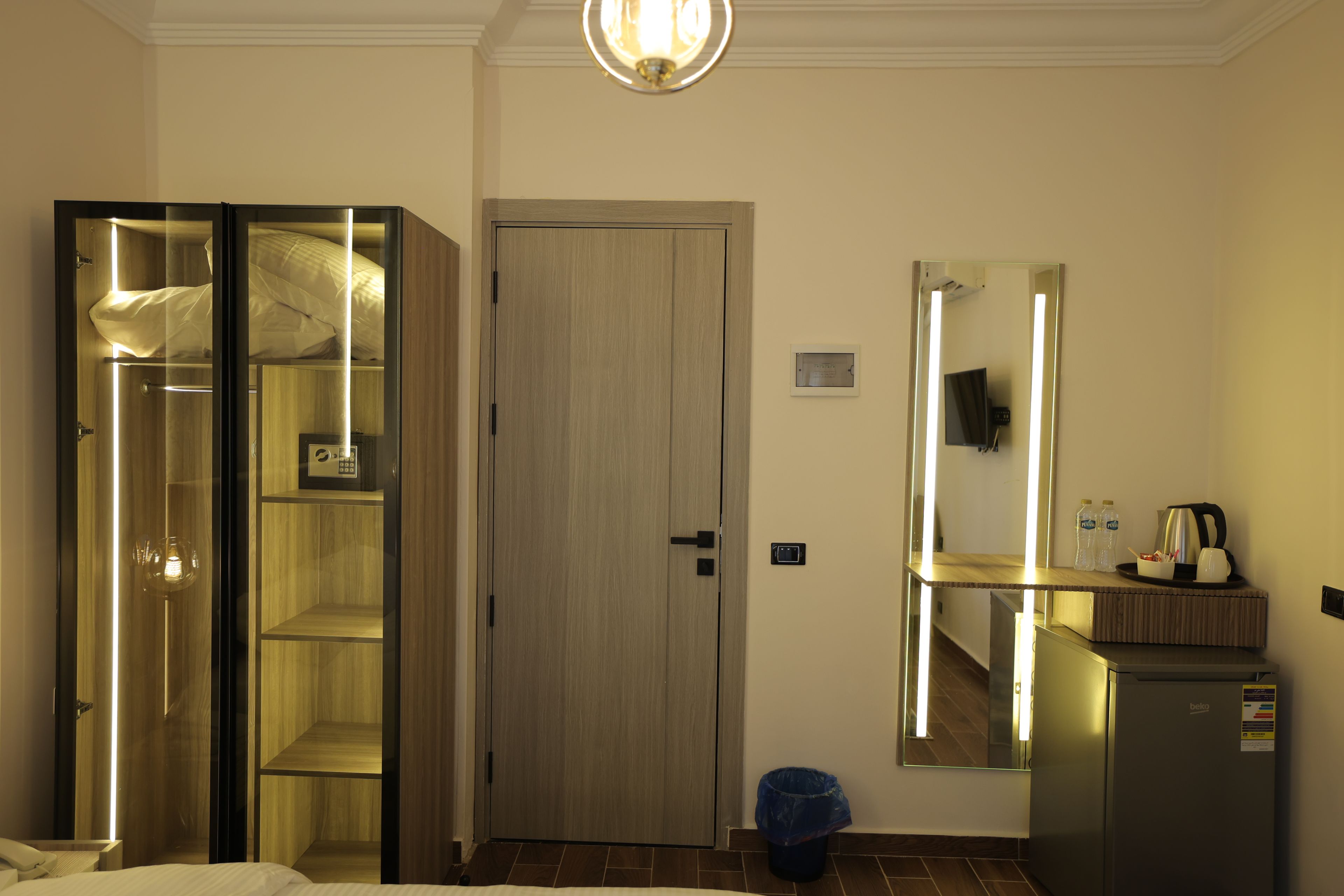 Ein Hotelzimmer mit Schrank, Tür, Spiegel, einem kleinen Tisch mit Wasserkocher und einem Mülleimer.