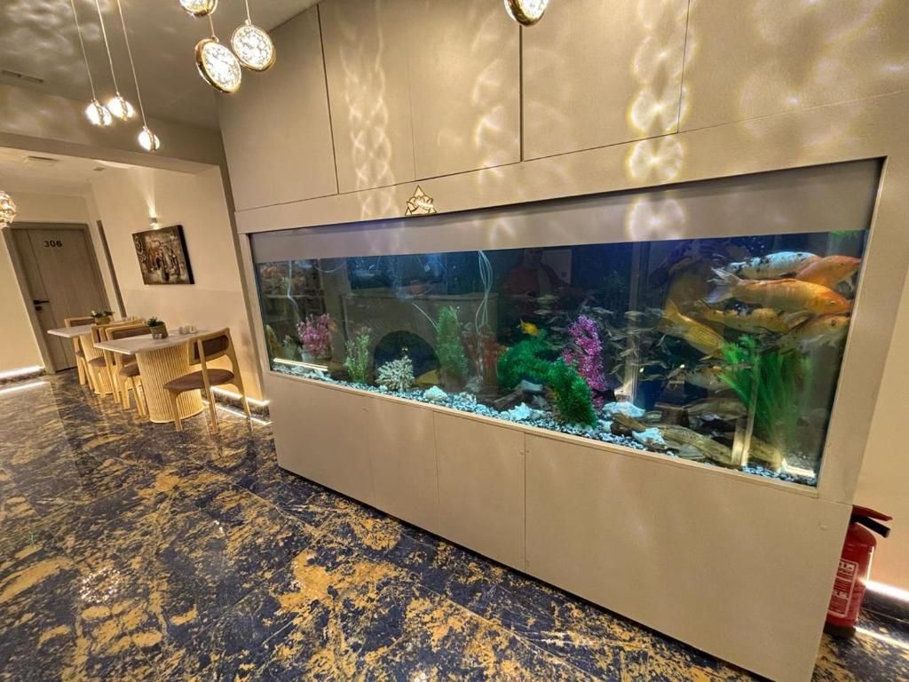 A large aquarium with various fish and aquatic plants, a marble-tiled floor, and a seating area with tables and chairs.