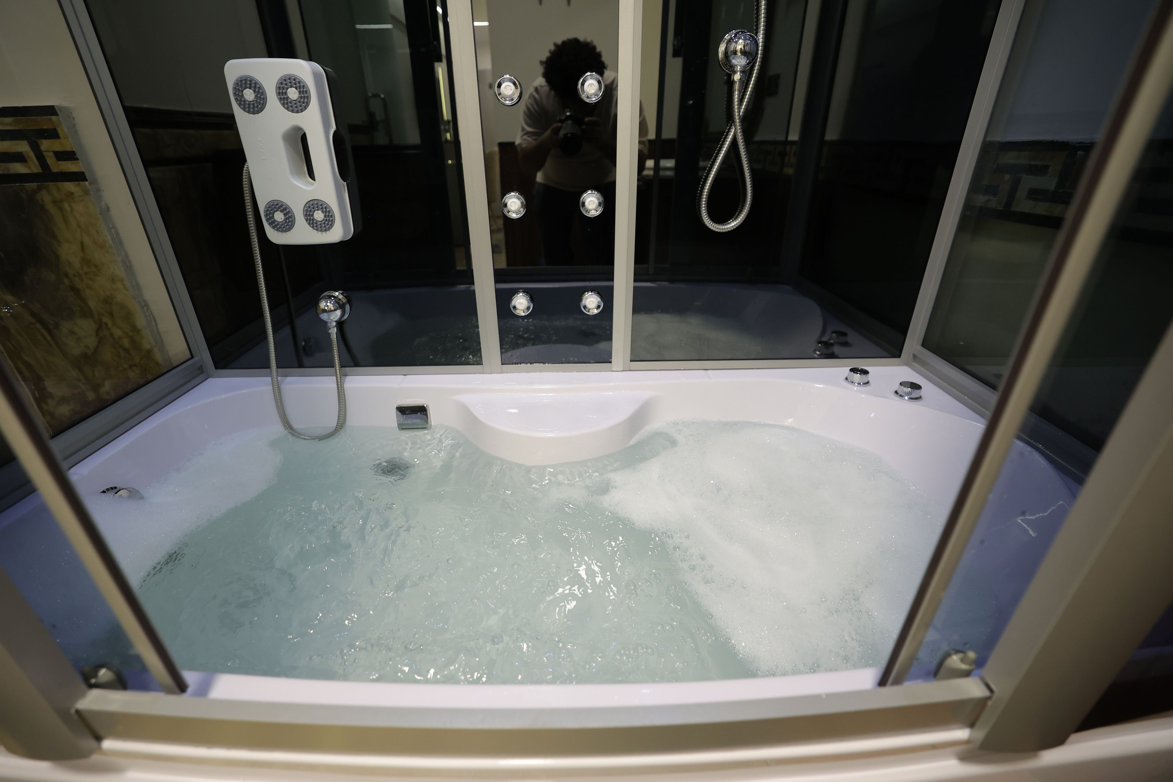 A hot tub with a built-in seat, a control panel with buttons, and a showerhead.