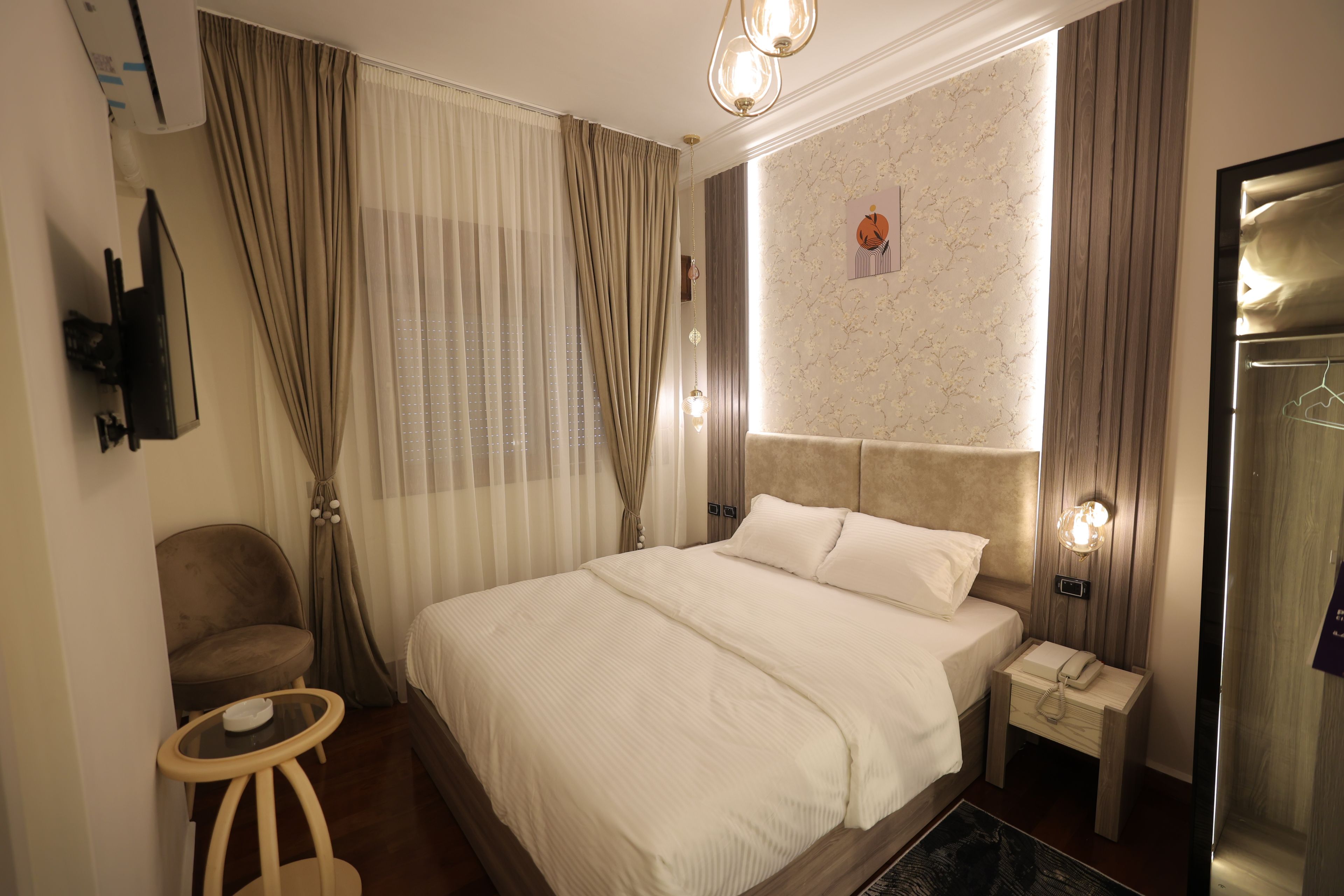 Habitación de hotel con cama, una silla, una mesita, una mesita de noche con teléfono y televisor montado en la pared.
