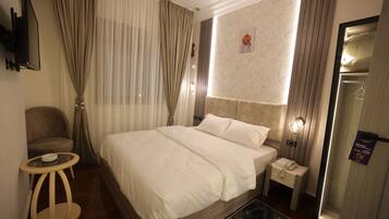 A hotel room with a large bed, a bedside table with a lamp, a chair, and a television mounted on the wall.