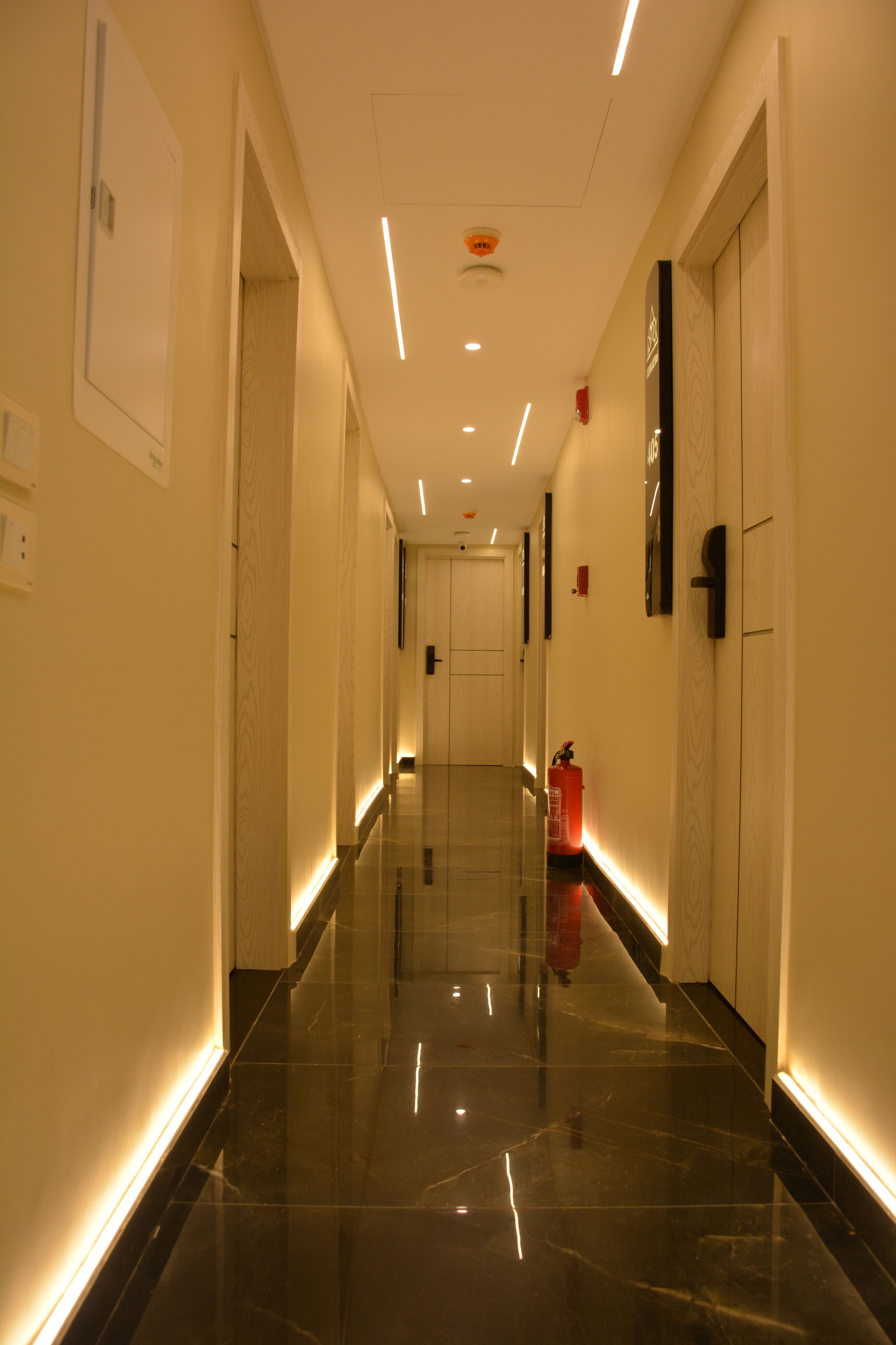 A corridor with a polished floor, doors on both sides, and a fire extinguisher mounted on the wall.