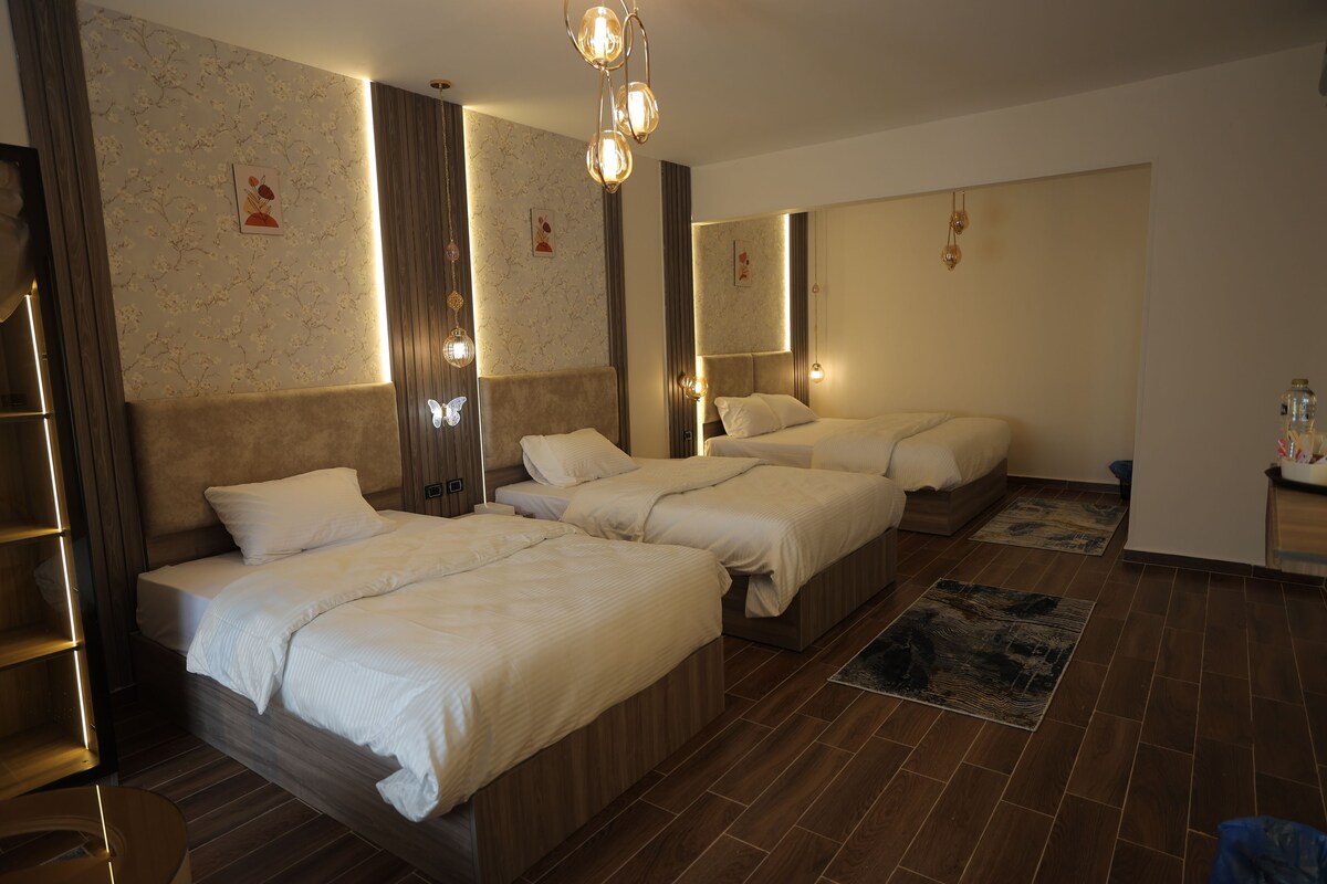 Habitación de hotel con tres camas, suelo de madera e iluminación en la pared.