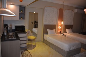 Habitación de hotel con kitchenette, cama con dos almohadas, una silla y mesita de noche con lámpara.