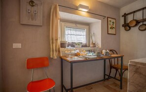 Cocina compacta con una mesa de comedor, sillas, ventana con cortinas y un colgador de ollas en la pared.