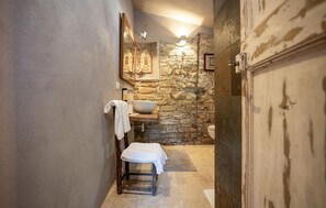 Un baño con pared de piedra, un lavabo blanco, un perchero y un banco de madera.