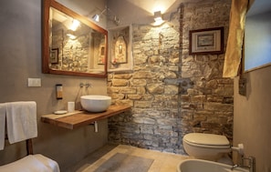 Een badkamer met een stenen muur, een houten wastafelmeubel, een witte wastafel, een toilet en een bad.