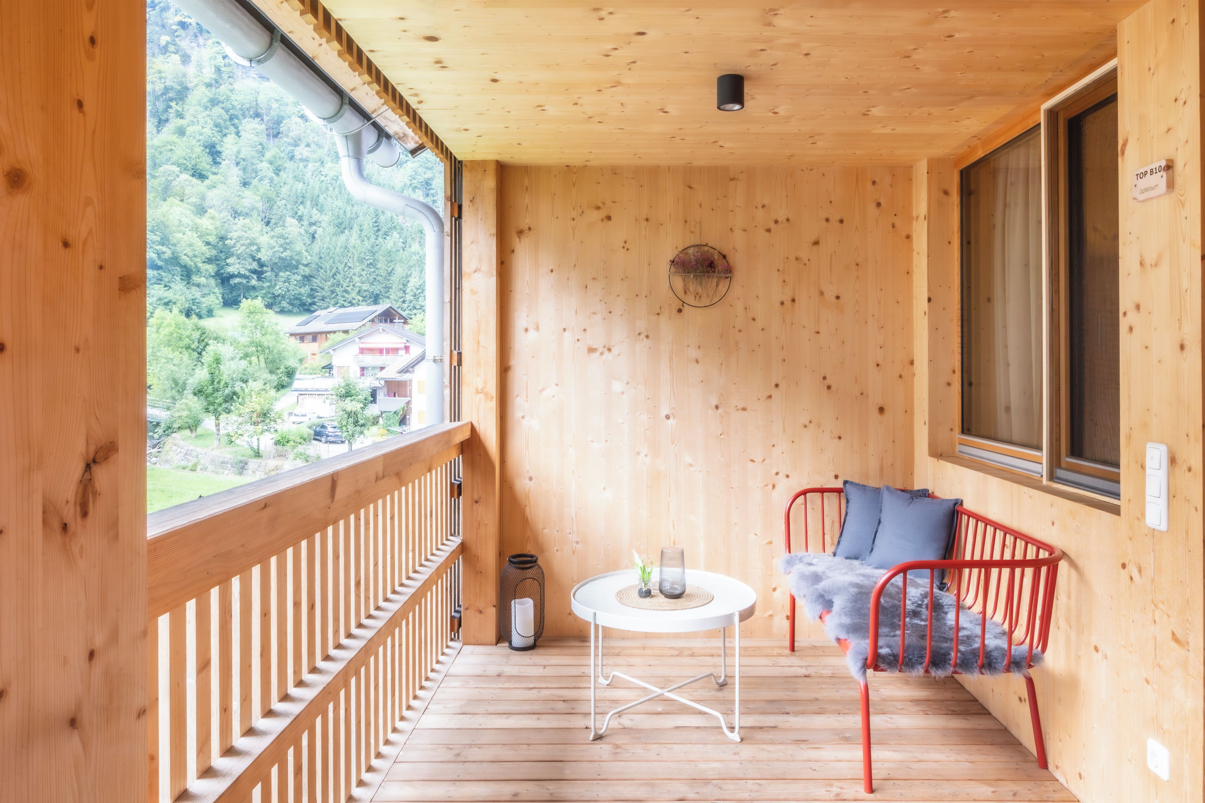 Ein Holzbalkon mit Blick auf ein bewaldetes Gebiet, ein runder Tisch mit einem Stuhl und ein Fenster mit einem Schild.