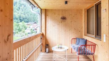 Ein Holzbalkon mit Blick auf ein bewaldetes Gebiet, ein runder Tisch mit einem Stuhl und ein Fenster mit einem Schild.