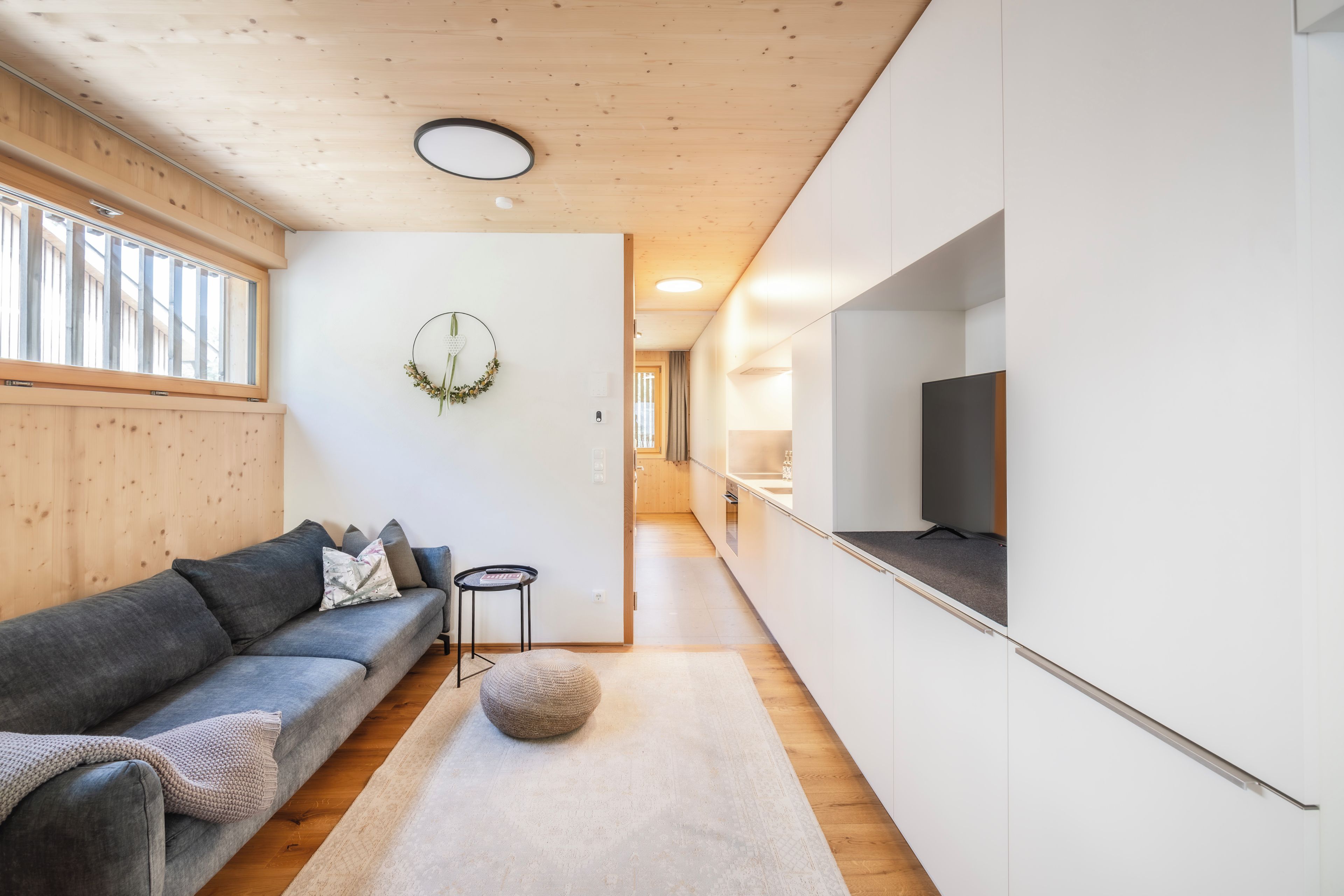 Ein modernes Wohnzimmer mit einem grauen Sofa, einem kleinen runden Tisch und einem dekorativen Kranz an der Wand.