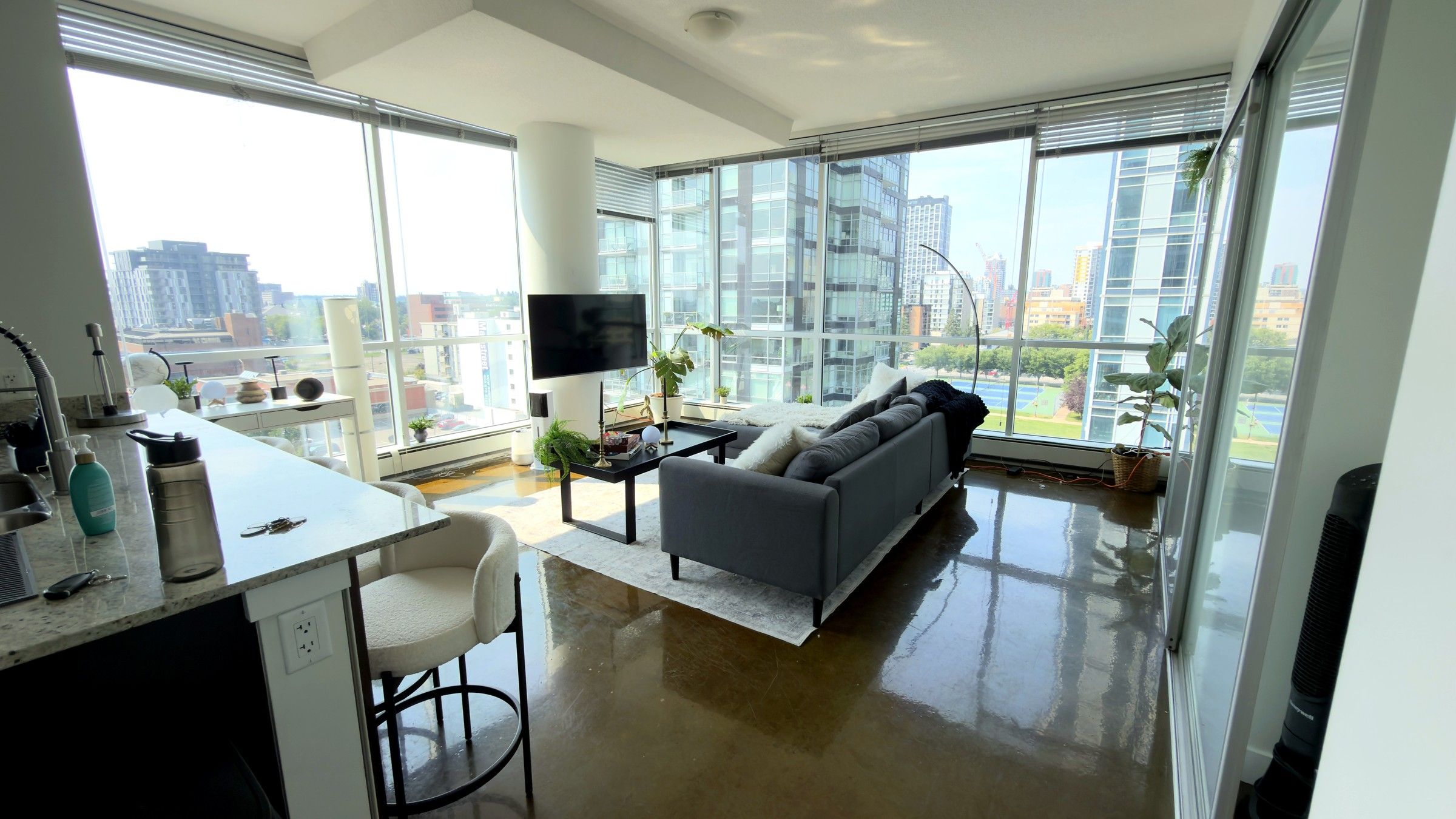 A modern living room with a sofa, a dining area with a table and chairs, and large windows offering a city view.
