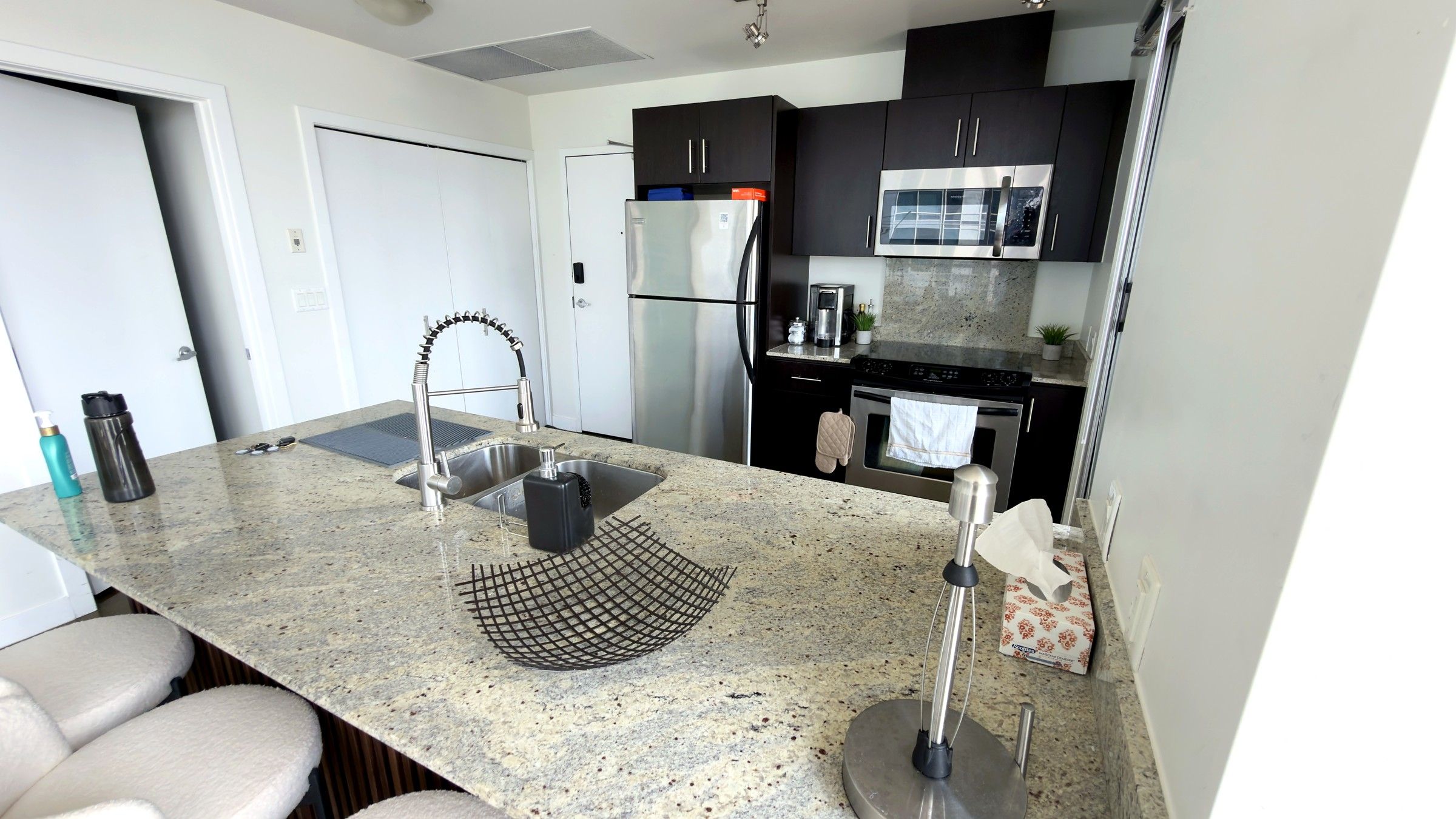 A modern kitchen with granite countertops, stainless steel appliances, and a central island with a sink and a wire rack.