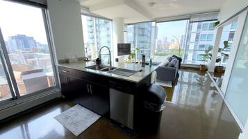 A modern kitchen with a large window, a built-in dishwasher, and a grey sofa in the living area.