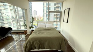 Quarto moderno com uma cama grande, uma planta em vaso e vista para edifícios altos.