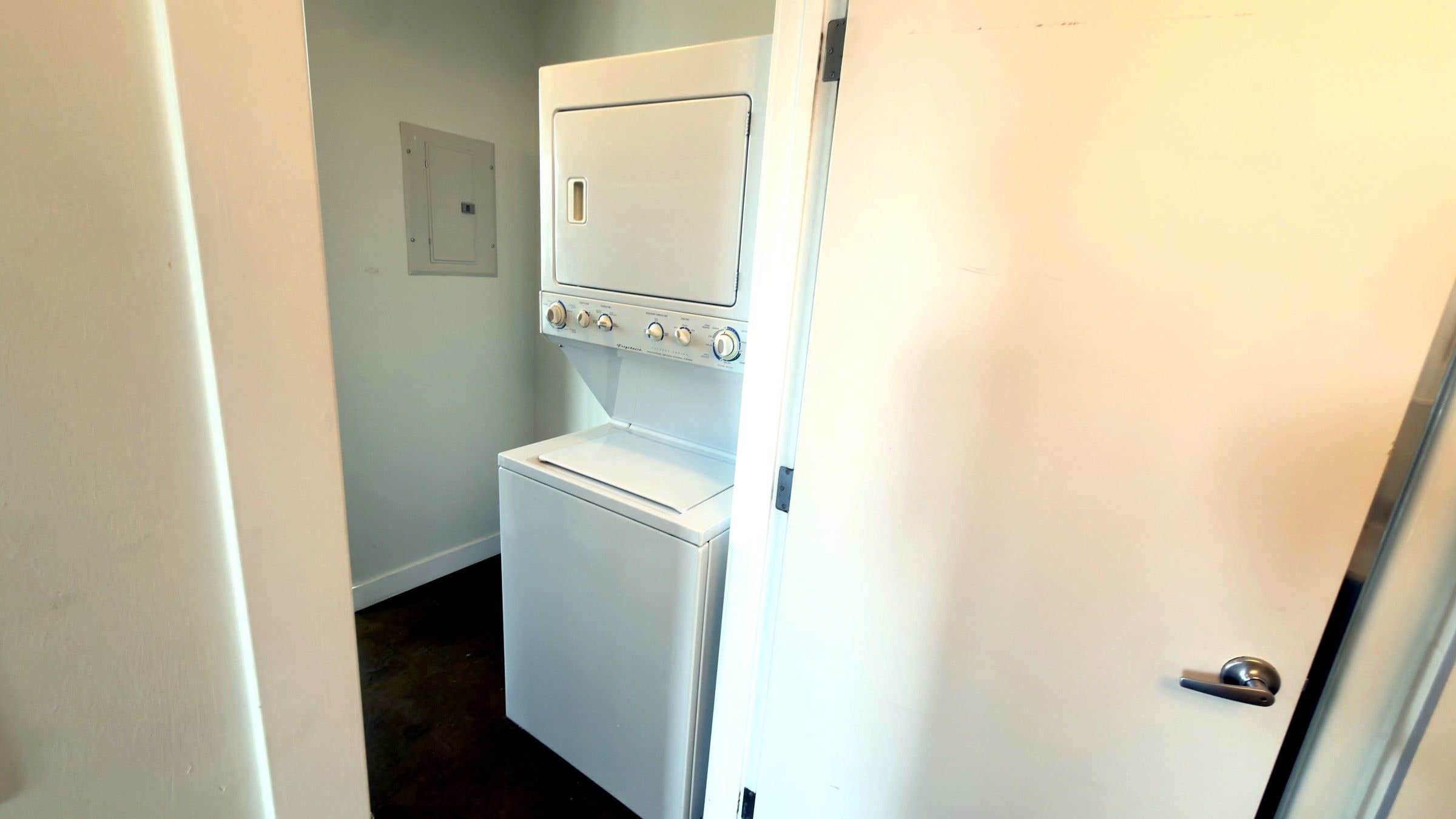 A compact laundry room with a washer and dryer, a door with a handle, and a light switch on the wall.