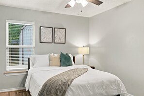 A bedroom with a bed, a window with blinds, a ceiling fan, and two wall-mounted picture frames. - Spacious 4BR Home, King Bed, Private Pool - NW OKC Near Quail Springs (Oklahoma City)