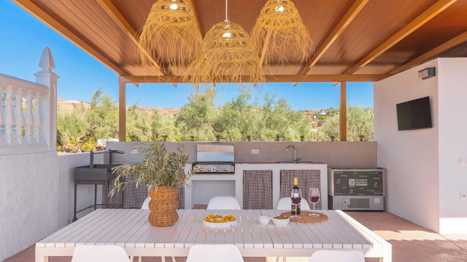An outdoor patio with a grill, a table set for dining, and a view of the surrounding landscape.