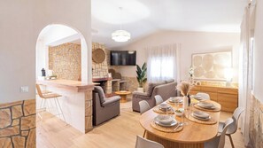 A modern living space with a stone accent wall, a flat-screen TV, a dining area with a round table set for four, and a cozy seating arrangement. - Atalaya del Torcal Antequera - La Higuera by Ruralidays (Málaga)