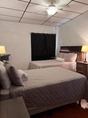 A hotel room with two beds, a ceiling fan, a window with curtains, and bedside lamps. - Gran Bonanza Hotel (ALEGRÍA)