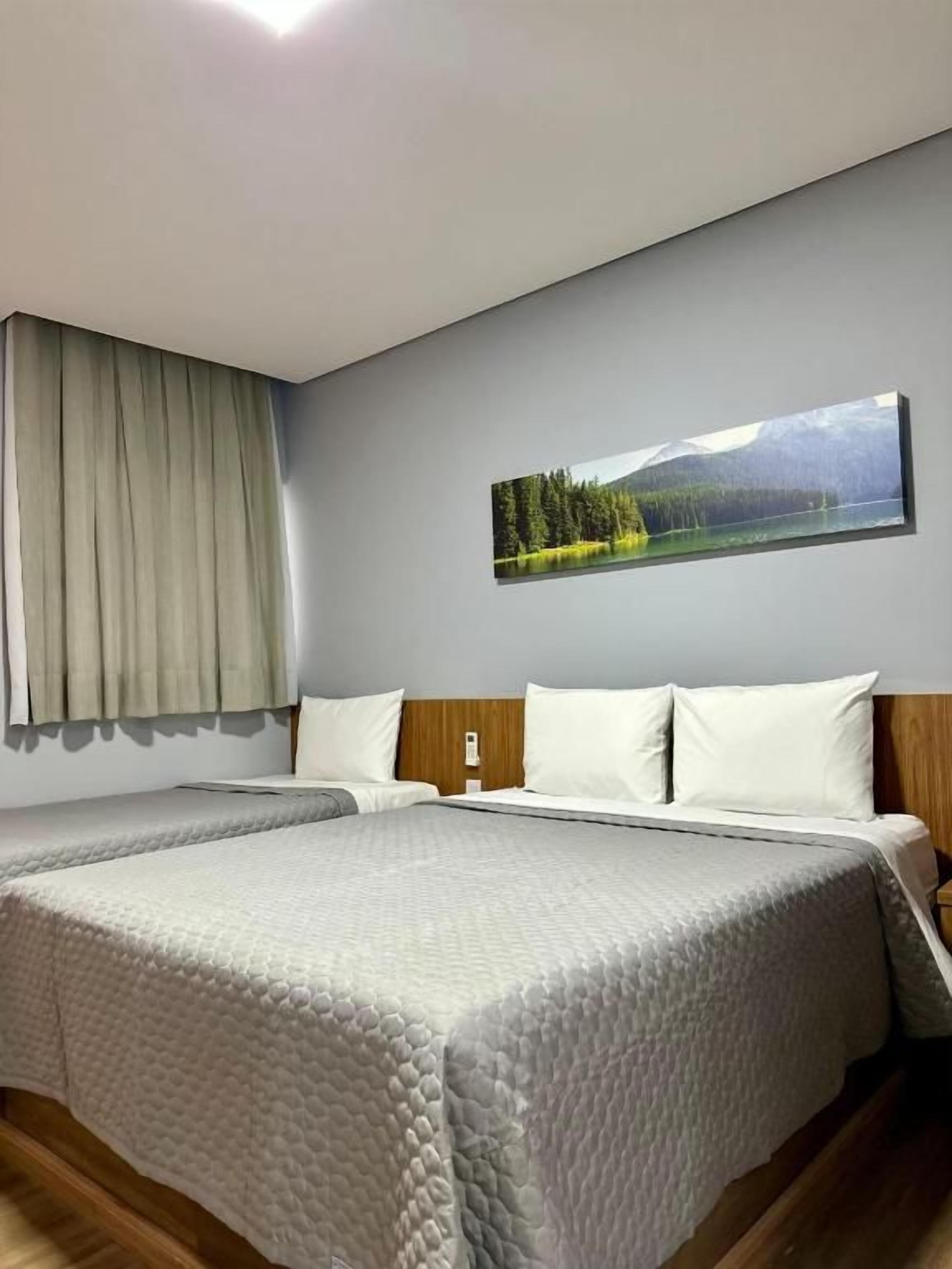 Habitación de hotel con dos camas, un cuadro de un paisaje y una ventana con cortinas.