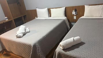 Dos camas con sábanas y almohadas blancas, un armario de madera y una mesita de noche con un cargador de teléfono.