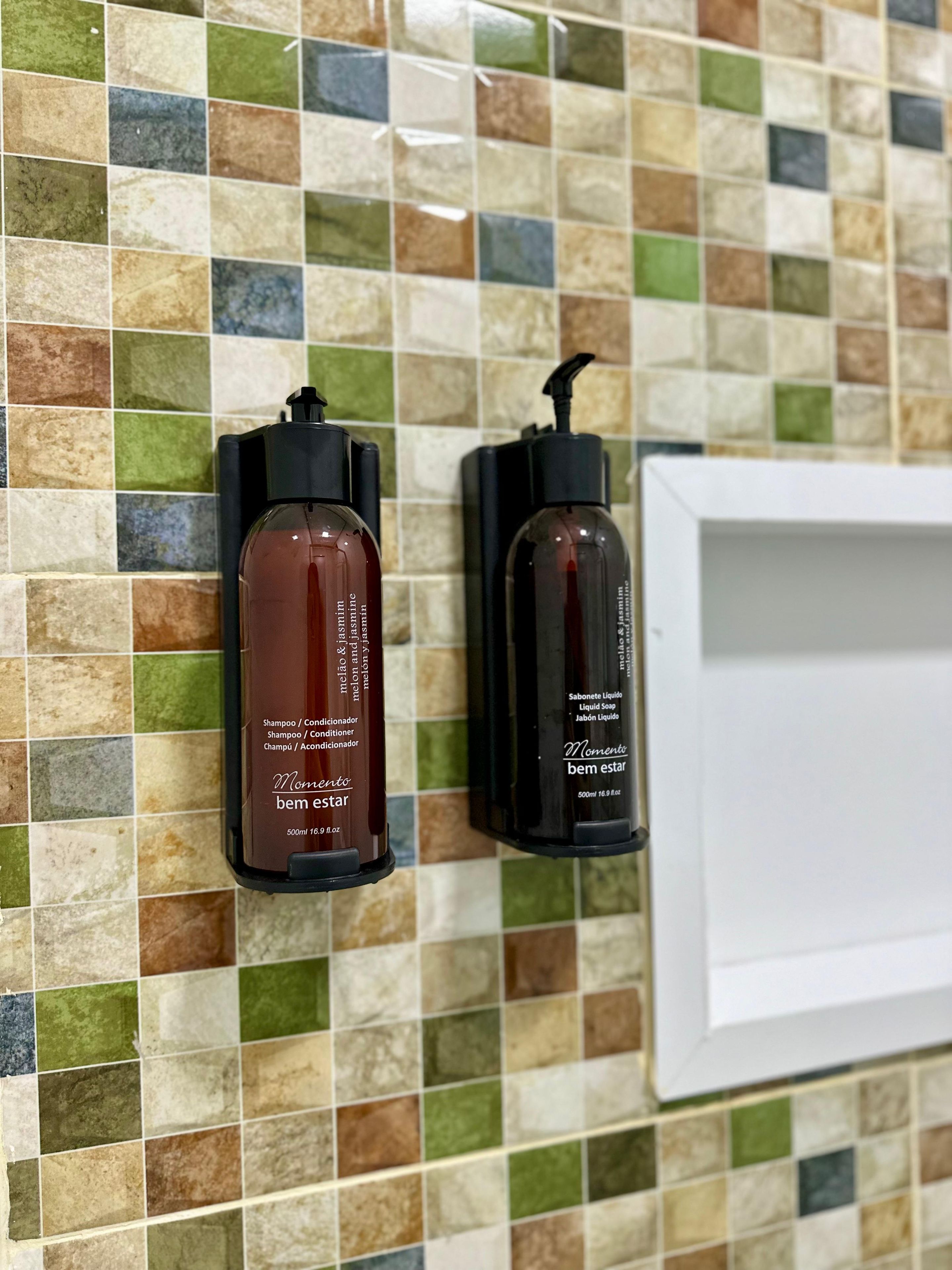 Dos botellas de champú y acondicionador sobre una pared de baldosas.