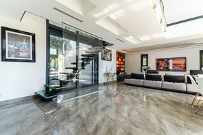 A modern living room with a glass staircase, a sofa set, and a large painting. - Villa Les Vagues • Pool, hot tub & beach 500 m away (Agde)