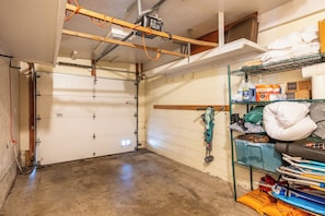 A garage with a concrete floor, a white garage door, and a metal shelving unit on the right. - North Mission Beach House - Patio + Garage (San Diego)