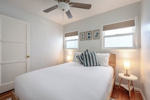 Une chambre à coucher avec un lit, deux lampes de chevet, un ventilateur de plafond et une porte.