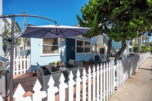 A residential property with a fenced yard, a patio with outdoor furniture, and a clear blue sky. - North Mission Beach House - Patio + Garage (San Diego)