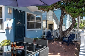 A patio area with outdoor seating, a table with food and drinks, and a blue building with a white fence. - North Mission Beach House - Patio + Garage (San Diego)