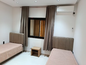 A room with two beds, a small table, an air conditioning unit, and a window with curtains. - Eline House (Hammamet)