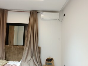 A bedroom with a bed, a window with curtains, an air conditioning unit, and a bag on the floor. - Eline House (Hammamet)