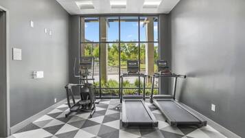 A gym with treadmills, an elliptical, and a stationary bike, with large windows and a geometric patterned floor.